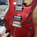 červená elektrická kytara s lesklým povrchem a hmatníkem z tmavého dřeva. Nástroj má dva humbuckery, chromovaný tremolo systém a tři černé ovládací k…