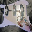 Bílá pickguard pro elektrickou kytaru s namontovanými třemi snímači a elektroinstalací. Snímače jsou černé, prostřední je v provedení s viditelnými p…
