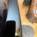 Detailní pohled na černý, lesklý povrch hudebního nástroje. Na hraně je viditelná prasklina v laku a několik drobných škrábanců. Žádné značky ani náp…
