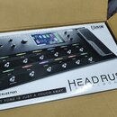 Fotografie znázorňuje krabici s kytarovým procesorem HeadRush Pedalboard v černé barvě. Na zařízení je vidět displej, několik ovládacích knoflíků a ř…