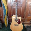 Akustická kytara s cutawayem v přirozené dřevěné barvě a červeným puntovaným pickguardem. Na hlavě hmatníku je viditelné logo Epiphone. Hmatník obsah…