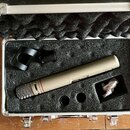 V hliníkovém kufru s černou pěnovou výplní je umístěn kondenzátorový mikrofon v béžové barvě s kovovou síťkou. Na těle mikrofonu je viditelný nápis "…