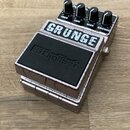 Kytarový efekt pedál s povrchem v imitaci prasklého stříbrného kovu. Na horní části je nápis GRUNGE a pod ním černý gumový panel s logem Digitech. Pe…