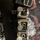 Tři stříbrné kovové triggery s černými plastovými panely a bílým nápisem RT-3T Tom Trigger OUTPUT. Nad nimi je umístěn černý plastový držák s bílým l…