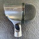 Stříbrný dynamický mikrofon s kovovou síťkou. Na těle je viditelný nápis "ALON" a pod ním nečitelná řada znaků. Povrch mikrofonu vykazuje známky opot…