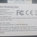 Fotografie detailu bílé štítku s technickými údaji na přístroji. Je zde uveden název Mini Modeling Amp, Model: Mighty Lite BT a Trademark: NUX. Štíte…