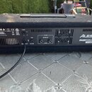 Zadní strana černého mixážního pultu s texturovaným povrchem a kovovou rukojetí. Na pravé straně je bílý nápis ALESIS a pod ním model PA80 80-WATT 4-…