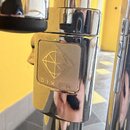 Detail chromovaného kovového komponentu s čtvercovým logem. Na logu je vyryto geometrické znázornění kosočtverců a nápis DIXON. Povrch je lesklý s vi…