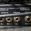 Detail zadní části černého hudebního přístroje s kovovými konektory. Na šasi je bílý nápis A PRODUCT OF PEAVEY ELECTRONICS CORP. MERIDIAN, MS MADE IN…