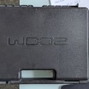Černý plastový kufřík s texturovaným povrchem. Uprostřed víka je vyražen nápis WX02. Povrch vykazuje lehké známky opotřebení a prach.