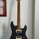 Černá elektrická kytara s matným povrchem a zlatým hardwarem. Na hlavě hmatníku je viditelné logo "Cort". Nástroj má dva humbuckery a zlatý most. Kyt…