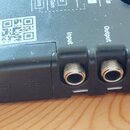 Detailní pohled na spodní hranu černého elektronického zařízení. Jsou zde tři konektory s nápisy Input, Output a Insert. Na boku je umístěn čtvercový…