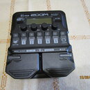 Černý multi-efektový procesor s nápisy G1 FOUR, ZOOM a Multi-Effects Processor. Zařízení obsahuje displej, čtyři ovládací knoflíky s popisky Lo, Mid,…