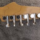 Detail hlavy kytary z jasného dřeva se šesti chromovanými ladicími mechanismy. Na tří levých mechanismech jsou černé krytky s bílým nápisem „Ibanez“.…