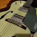 Světle zelená polodubová elektrická kytara s tmavě zeleným plechtrátorem. Na plechtrátoru je viditelný bílý nápis GRETSCH. Nástroj má dva snímače s k…