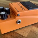 Kytarový efekt pedál oranžové barvy s černým spínacím tlačítkem. Na horní části je nápis Distortion DS-1 a logo BOSS. Na přední straně jsou tři černé…