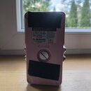 Zadní strana růžového efekt pedálu s dvěma černými sametovými plátny pro přilnutí. Na spodní části je víčko baterie s nápisem BATTERY a šroubem. Na h…