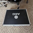Černý transportní kufr s hliníkovým profilem a uzavíracími zámky. Na horní straně je bílé logo a nápis AKG. V horní části fotografie je vidět část če…