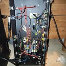 Fotografie zachycuje vnitřek černého elektronického zařízení s odhalenou zapojovací strukturou. Jsou vidět různobarevné vodiče, potenciometry, konden…