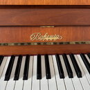 Detail klavíru z dřeva s hnědým povrchem. Nad klávesami je umístěno zlaté nápisové logo „Bohemia PIANOS“. Klávesnice je v klasickém černobílém proved…