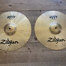 Dvě mosazné činely značky Zildjian s viditelným rakováním. Levý činel nese nápisy ZHT a Mastersound Hihat Bottom 13"/33 cm. Pravý činel má nápisy ZHT…