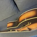 Detailní pohled na korpus polodubové nebo archtop elektrické kytary s barvou sunburst. Nástroj má žlutý lem a f-otvor v těle. Povrch laku vykazuje vi…