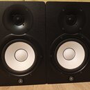 Dva černé studiové monitory s bílými membránami basových reproduktorů. V dolní části obou reproduktorů je umístěno kulaté logo Yamaha. Povrch korpusů…