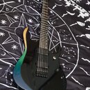 Elektrická kytara s černým bodies, které má na horním vyřezu přechod barev od dřevěné přes zelenou až po modrou. Nástroj má dva humbuckery, jeden ovl…