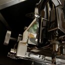 Detailní pohled na chromované kovové části hudebního nástroje, pravděpodobně mechanismus ladění nebo most. Na jednom z kovových dílů je vyryto logo z…