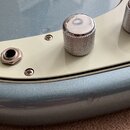 Detailní pohled na část těla elektrokitary v modré barvě s krémovým pickguardem. Na povrchu jsou vidět dva kovové knofíky s rýhovaným povrchem a něko…