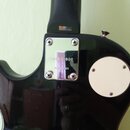 Detail zadní strany černé elektrické kytary v místě spoje krku s tělem. Na kovovém krytu je vyražen nápis S94030400 a pod ním text MADE IN KOREA. Pov…