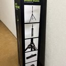 Kartonová krabice s produktem značky Gravity, na které je nápis „SET OF 2 SPEAKER STANDS WITH TRANSPORT BAG“. Na povrchu jsou fotografie černých repr…
