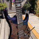 Tmavě fialová elektrická kytara s lesklým povrchem a viditelnou strukturou dřeva. Na hmatníku je vložka s logem „Schecter“ a nápisem „MODEL CUSTOM“.…