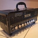 Černý kytarový kombozesilovač s kovovou mřížkou a nápisem VOX na přední straně. Na ovládacím panelu jsou bílé popisky INPUT, GAIN, VOLUME, TREBLE, MI…
