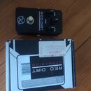 Černý efekt pedál s nápisy RED DIRT GERMANIUM a popisky ovládacích prvků GAIN, TONE a LEVEL. Na levé straně je bílé logo s písmenem R v kruhu. Vedle…