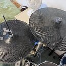 Dvě černé perforované činely s hustou sítí malých otvorů po celém povrchu. Na levém činely je vlevo viditelný bílý nápis MEHANIK. Oba nástroje jsou o…
