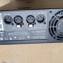 Zadní strana černého elektronického zařízení s ventilátorem a konektory. Jsou zde čtyři kruhové konektory označené jako CH2 LINK / OUT, CH2 IN, CH1 I…