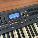 Černý MIDI kontrolér s klávesnicí. Na přístroji je modrý displej s nápisy „CC# 105“, „41“ a pod ním bílé logo „novation“. Vedle displeje jsou ovládac…