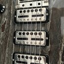 Detail elektrické kytary s tmavým, žilnatým povrchem. Na fotce jsou vidět tři chromované humbuckery a část mostu sstrunami. Nástroj nemá žádné vidite…