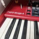 Červený digitální klavír s bílými a černými klávesami. Na červeném povrchu je bílý nápis nord stage 4 a pod ním menší text HAMMER ACTION 73. Vedle kl…