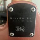 Detail zadní strany krku elektrické kytary s hnědým lakem a černým krytem uSpojení. Na krytu je nápis SILVER SKY a pod ním menší text JOHN MAYER MODE…