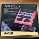 Krabice s produktem JAM BUDDY, což je Dual channel 2x4W pedal guitar amp. Na obalu je zobrazen červený pedál s ovládacími prvky a logo JOYO s nápisem…