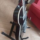 Tmavě červená polodupatá elektrická kytara s bílým lemováním korpusu, umístěná na černém stojanu. Nástroj má chromovaný hardware apáčku a ladicí knof…
