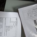 Fotografie zachycuje část dokumentu s textem a plastový obal s uživatelskou příručkou. Na příručce je črtný nákres zařízení s nápisy ZOOM a H6 handy…