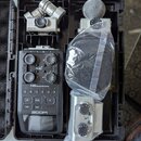 Černý plastový kufřík s polstrováním obsahuje digitální záznamák a tři vyměnitelné kapsle mikrofonů. Na přístroji je nápis H6 Handy Recorder a logo Z…