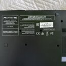 Fotografie zachycuje spodní stranu černého zařízení s několika nálepkami. Na levé straně je bílý nápis Pioneer DJ, pod ním text DJ CONTROLLER MODEL D…