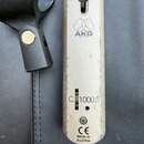 Detailní pohled na stříbrný kovový mikrofon. Na těle je vidět logo a nápis AKG, označení modelu C 1000 S, značka CE a nápis MADE IN AUSTRIA. Povrch v…