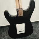 Zadní strana černé elektrické kytary s krkem z přírodního dřeva. Na kovém spojovacímdesce u krku je vyryto logo Squier a pod ním malý čtvercový symbo…