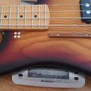 Detail elektrické basy s hmatníkem ze světlého dřeva a tělem v červeno-černém sunburst provedení. Na snímačích jsou viditelné nápisy DELANO a DELO. N…