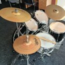 Černá bicí souprava s několika bubny a mosaznými činely. Na činelech je vidět nápis PAISTE, přičemž na jednom z nich je doplněno 2002. Bubny mají svě…